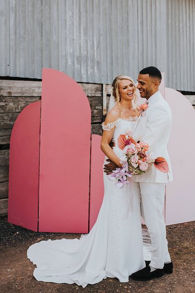 Bride and groom laugh together in front of their DIY pink wedding screen background.