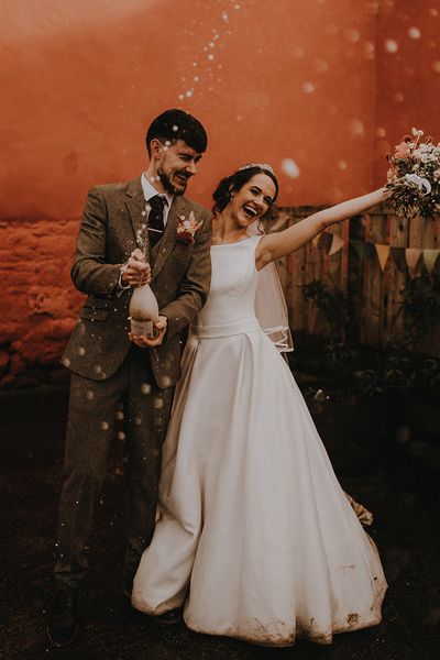 Rustic romance wedding theme for Devon wedding with the bride and groom popping champagne.