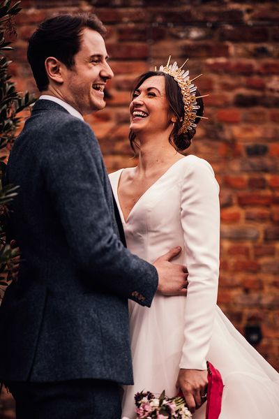 Bride in gold and crystal bride crown in layered wedding dress with groom in navy suit.