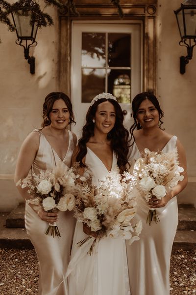 Bride in Alexandra Grecco wedding dress with white flower bridal headband and bridesmaids in champagne gold satin dresses.