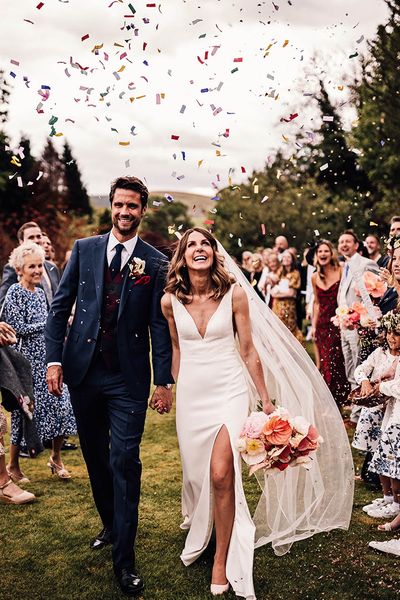 Bride in Suzanne Neville wedding dress with groom in blue suit have confetti exit from outdoor wedding at Rossie On The Earn venue. 