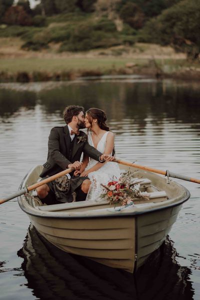 Bride in lace skirt wedding dress rides in boat with groom on the loch at the stunning Cardney Estate wedding venue.