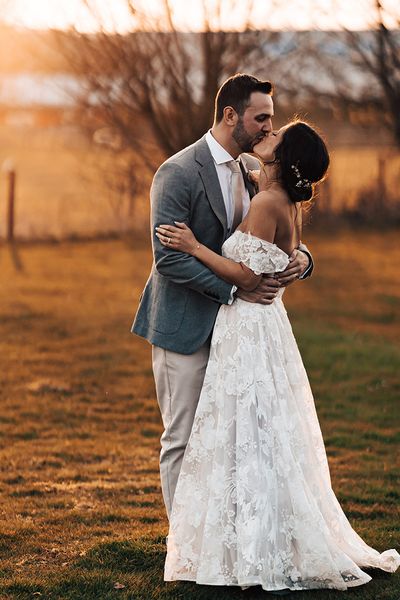 Bride in floral lace wedding dress with groom in grey suit share a kiss before their mariachi band wedding entertainment.