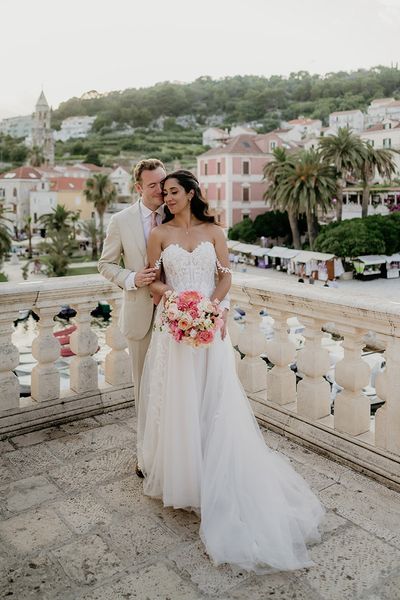 bride and groom stand on a balcony with Old Town Hvar in the background at destination wedding in Croatia 