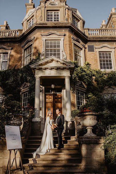 The bride and groom walk up the stairs at their wedding venue, Hampton Court House