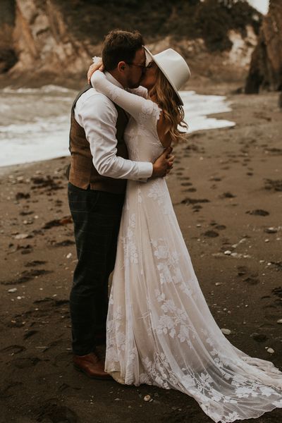 Seaside elopement with bride in a long sleeve lace wedding dress and fedora hat 