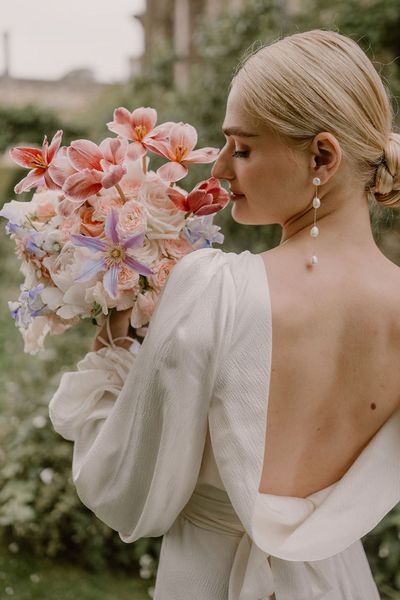 bride-in-open-back-wedding-dress-smelling-pink-wedding-bouquet-with-pearl-earrings