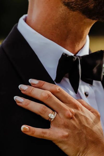 bride's hand on groom's chest with oval solitaire diamond engagement ring and chunky diamond wedding ring