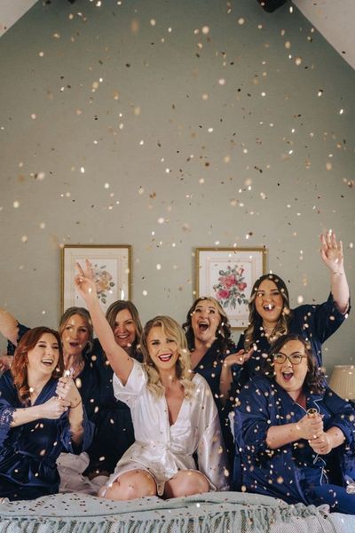 Bridesmaids in satin navy robes and pyjamas popping gold confetti canon as they get ready together