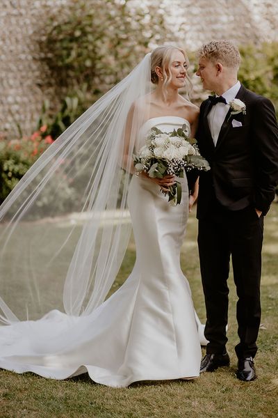 Mermaid wedding dress worn by the bride standing with groom in black tux