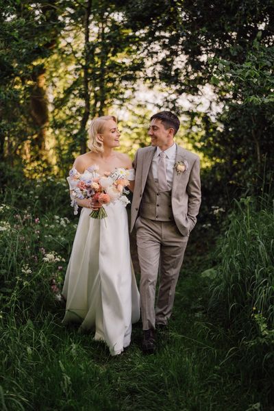 Bride & groom walking through forest as the sun sets