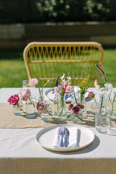 diy wedding centerpiece with mini glass vases and bottles and single stems of brightly coloured spring flowers on a linen tablecloth