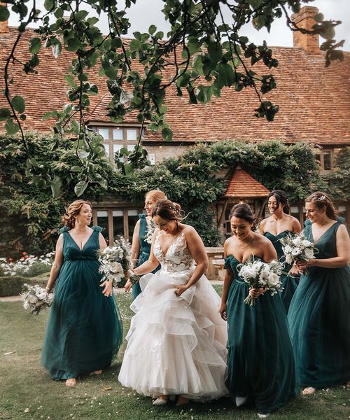 Bride in layered wedding dress walks with bridesmaids in green bridesmaid dresses