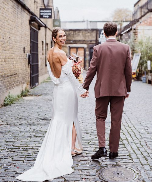 Bride in a cowl neck wedding dress walking with groom in a brown suit.