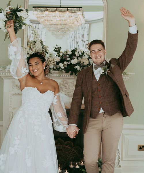 Bride in a floral wedding dress and the groom in a checkered suit in front of faux wedding flower decorations.