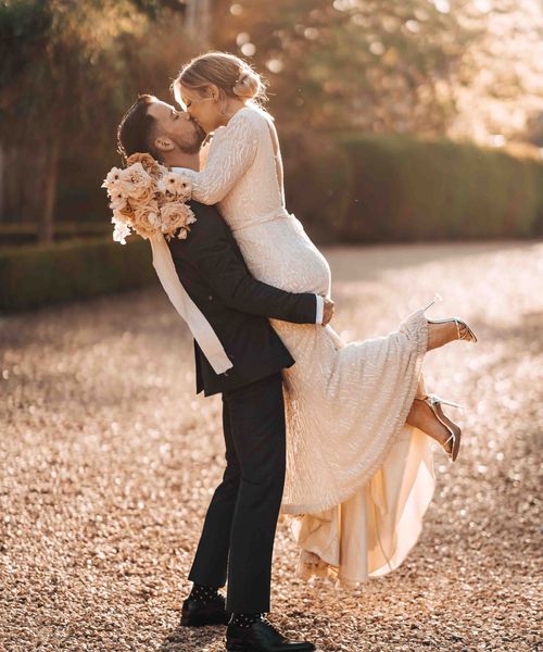 Bride in beaded wedding dress is picked up and kissed by the groom in front of Pennard House wedding venue.