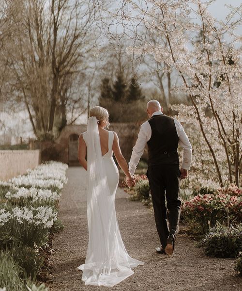 Bride in button back wedding dress from Made With Love walks holding hands with groom around Middleton Lodge for black tie wedding.