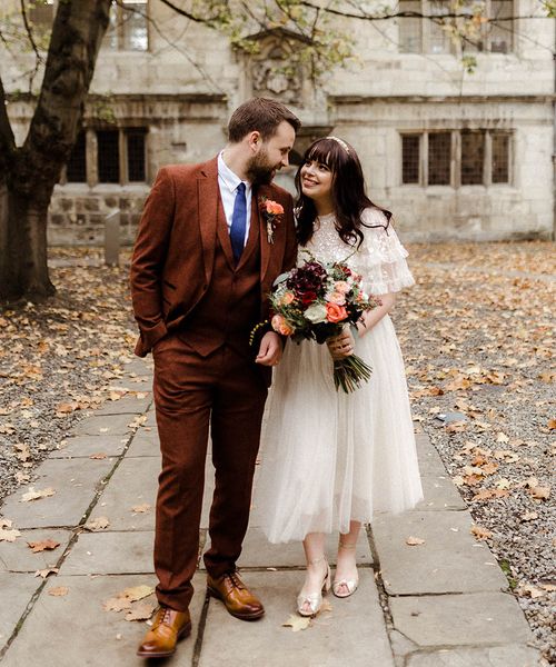 Bride in Needle and Thread top and skirt and groom in brown suit look into each other's eyes on their wedding day. 