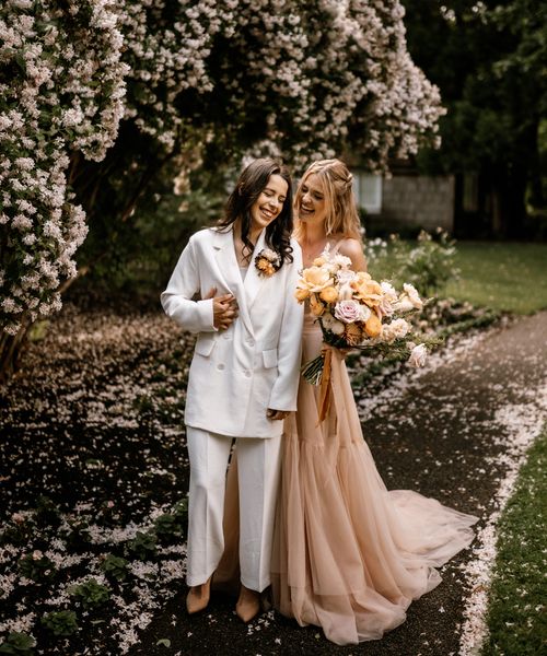 Honey yellow wedding inspiration with two brides in a peach wedding dress  and white bridal suit