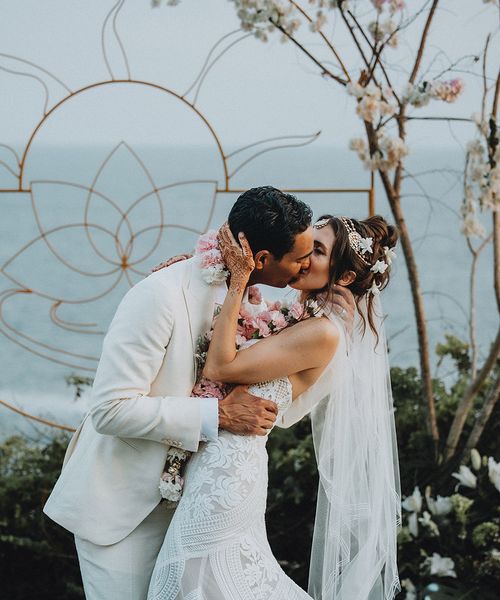 Groom in cream suit kisses bride in boho lace wedding dress and flower hair accessories at Tigre Del Mar wedding in Mexico