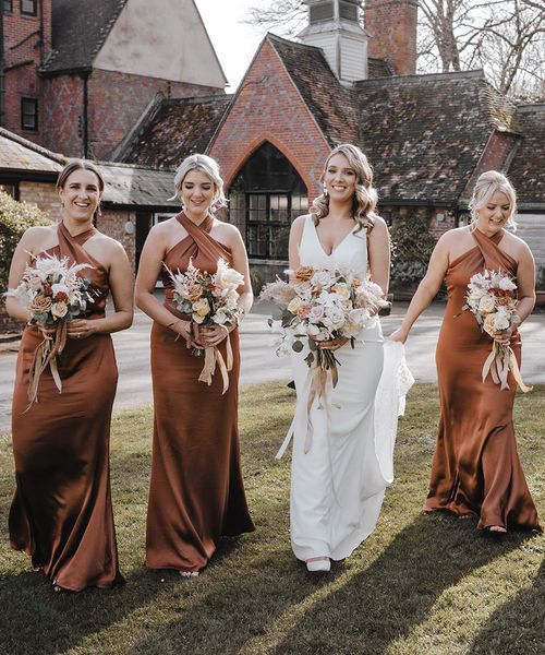 Bride walks with her bridesmaids in stunning satin halter neck copper bridesmaid dresses. 