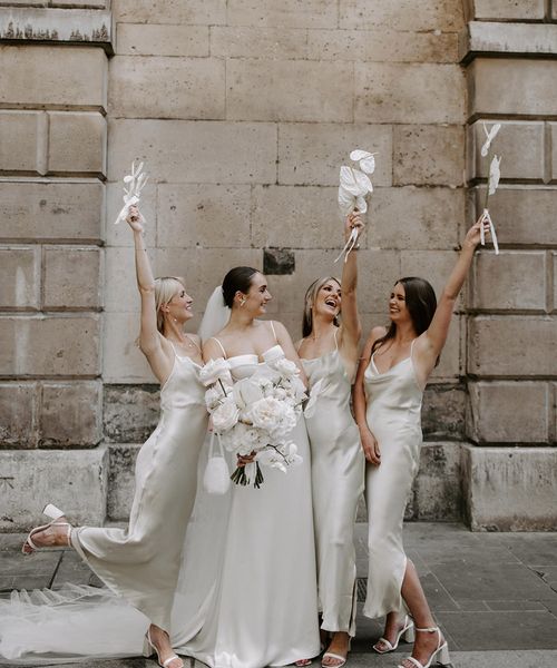 Bride holding white wedding bouquet with bridesmaids in white dresses.