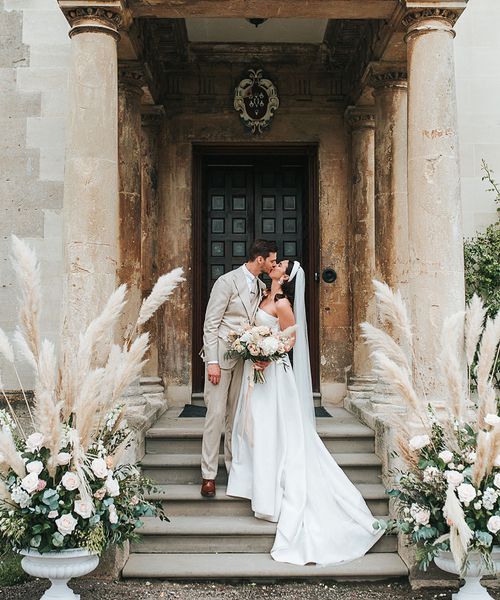 Bride in Jesus Peiro wedding dress and groom in beige suit with pampas grass floral arrangements. 