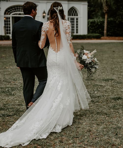 Bride in lace illusion back wedding dress walking holding hands with groom on their wedding day.