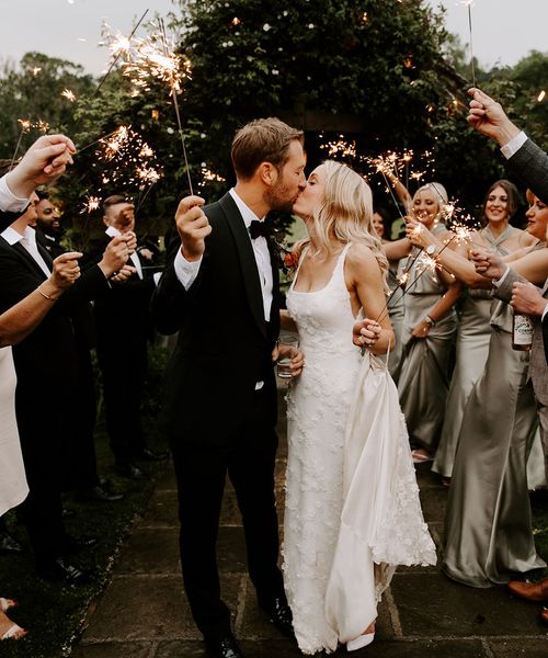 Bride in a 3D applique wedding dress with the groom sharing a kiss for their sparkler send off.