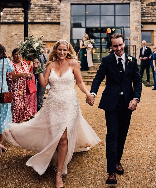 Bride in an Alexandra Grecco Lana wedding dress walking with the groom in a dark blue suit.