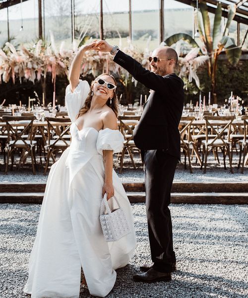 Bride carries a pearl handbag wearing sunglasses in a puff sleeve wedding dress with the groom also in sunglasses.