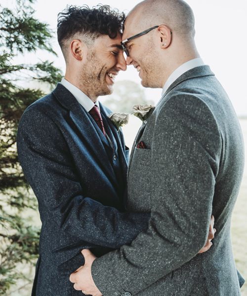 Grooms in blue and grey suit jackets with rose buttonholes made from pages from their favourite books for their DIY wood slice table centrepiece decor wedding.