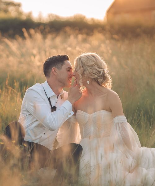 Bride and groom sitting in grass during golden hour at barn wedding