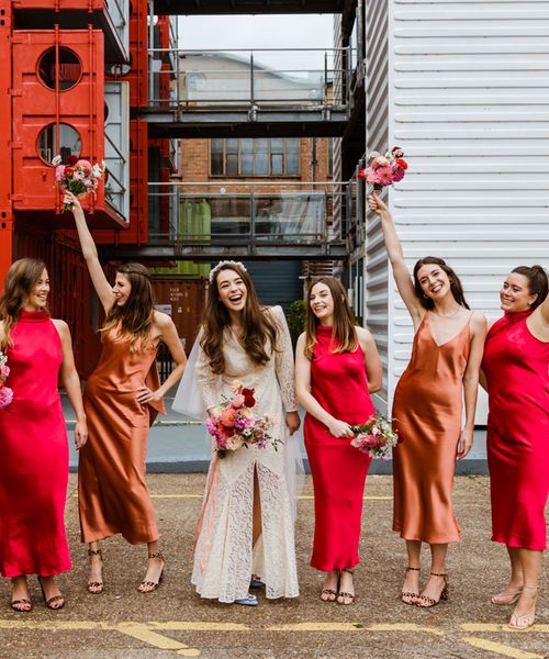 Trinity Buoy Wharf wedding with bride in a lace Rixo dress and bridesmaids in red and orange satin bridesmaid dresses