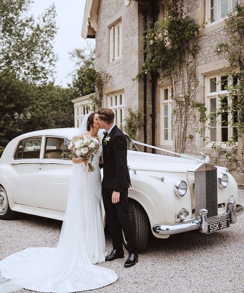 Bride and groom kissing in front of white wedding car at the Casterton Grange Estate venue.