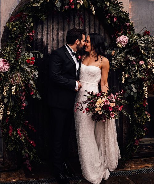 Bride in a beaded sparkle wedding dress with the groom in black tie surrounded by pink flowers.