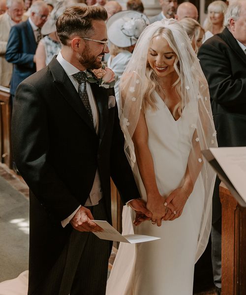 Bride wearing a flower applique veil standing with the groom for their church ceremony.