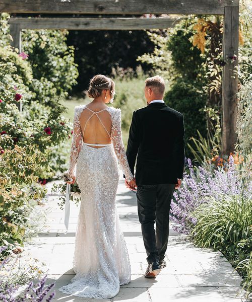 Bride in 3D lace wedding dress with an open back walking with the groom in black tie.