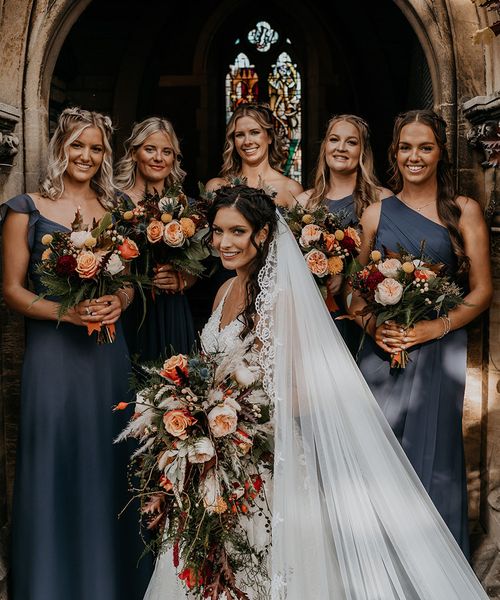 Bride holding cascade wedding bouquet with bridesmaids in navy blue dresses