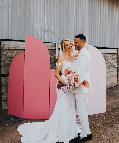 Bride and groom laugh together in front of their DIY pink wedding screen background.