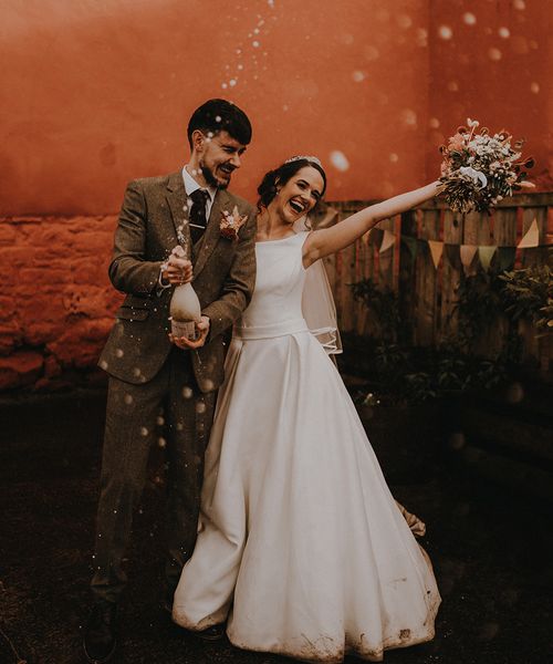 Rustic romance wedding theme for Devon wedding with the bride and groom popping champagne.