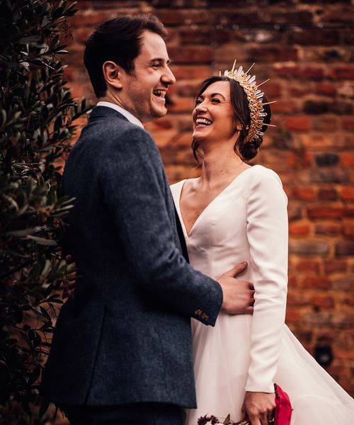 Bride in gold and crystal bride crown in layered wedding dress with groom in navy suit.