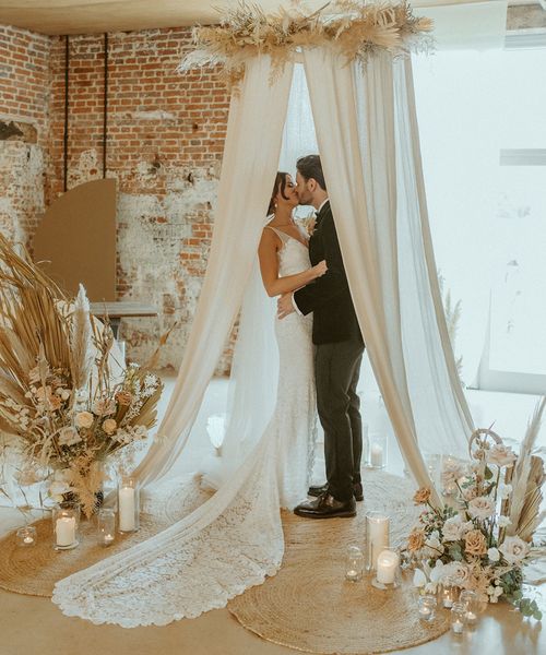 Bride and groom share a kiss under their wedding drapes at the altar decorated with candles at Godwick Barn. 