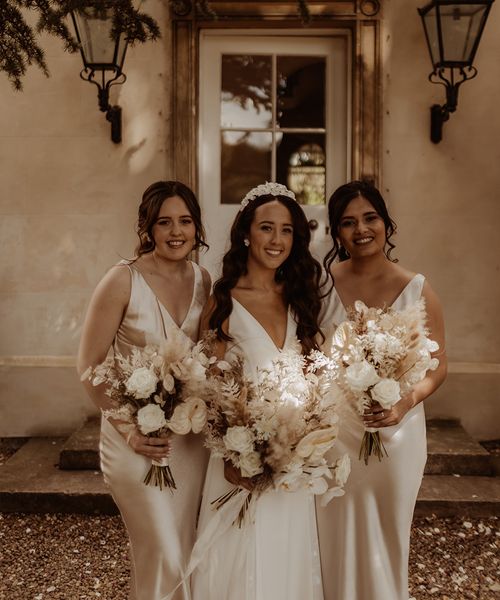 Bride in Alexandra Grecco wedding dress with white flower bridal headband and bridesmaids in champagne gold satin dresses.