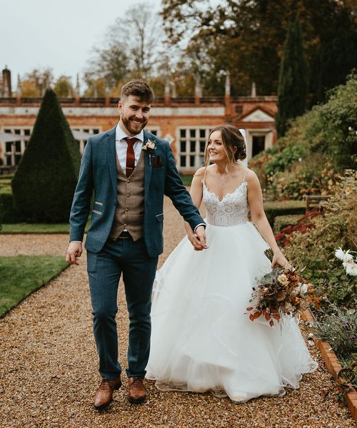 Bride in Blush by Hayley Paige holding autumnal wedding bouquet with groom in blue suit for Oxnead Hall wedding,