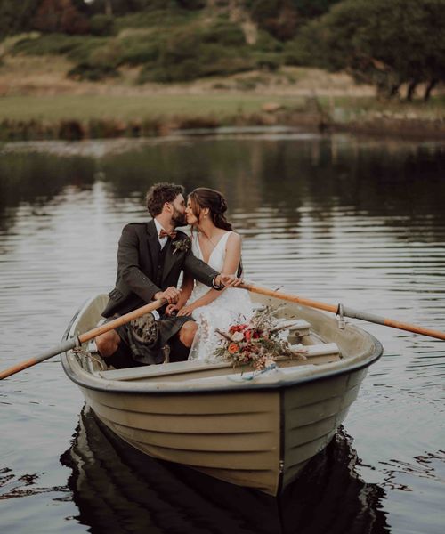 Bride in lace skirt wedding dress rides in boat with groom on the loch at the stunning Cardney Estate wedding venue.