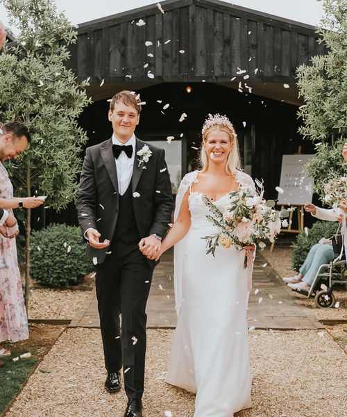 Bride in handmade wedding dress with crown walking with groom in black tie. 