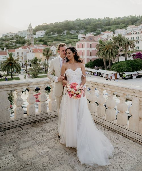 bride and groom stand on a balcony with Old Town Hvar in the background at destination wedding in Croatia 