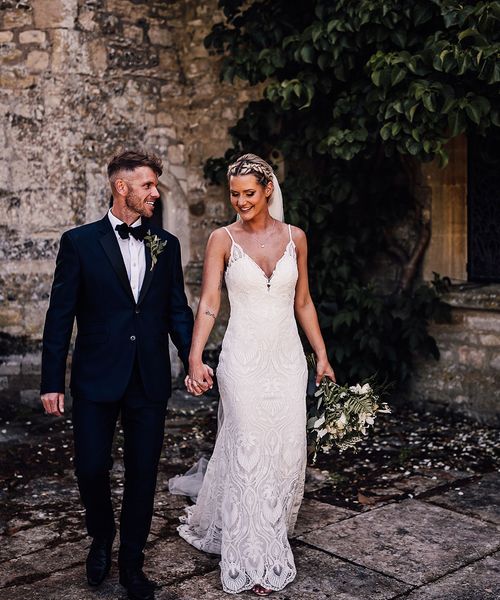 Bride in lace wedding dress and groom in black tie walk together at Athelhampton House.