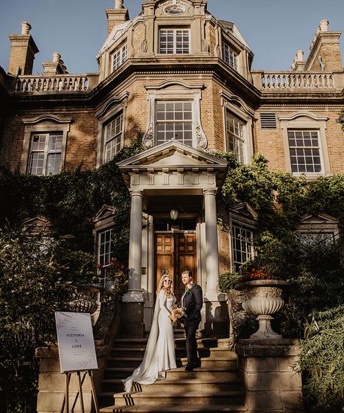 The bride and groom walk up the stairs at their wedding venue, Hampton Court House